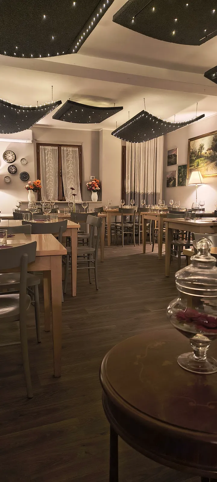 La sala dell’osteria di sera, con le luci soffuse sul soffitto e i tavoli apparecchiati