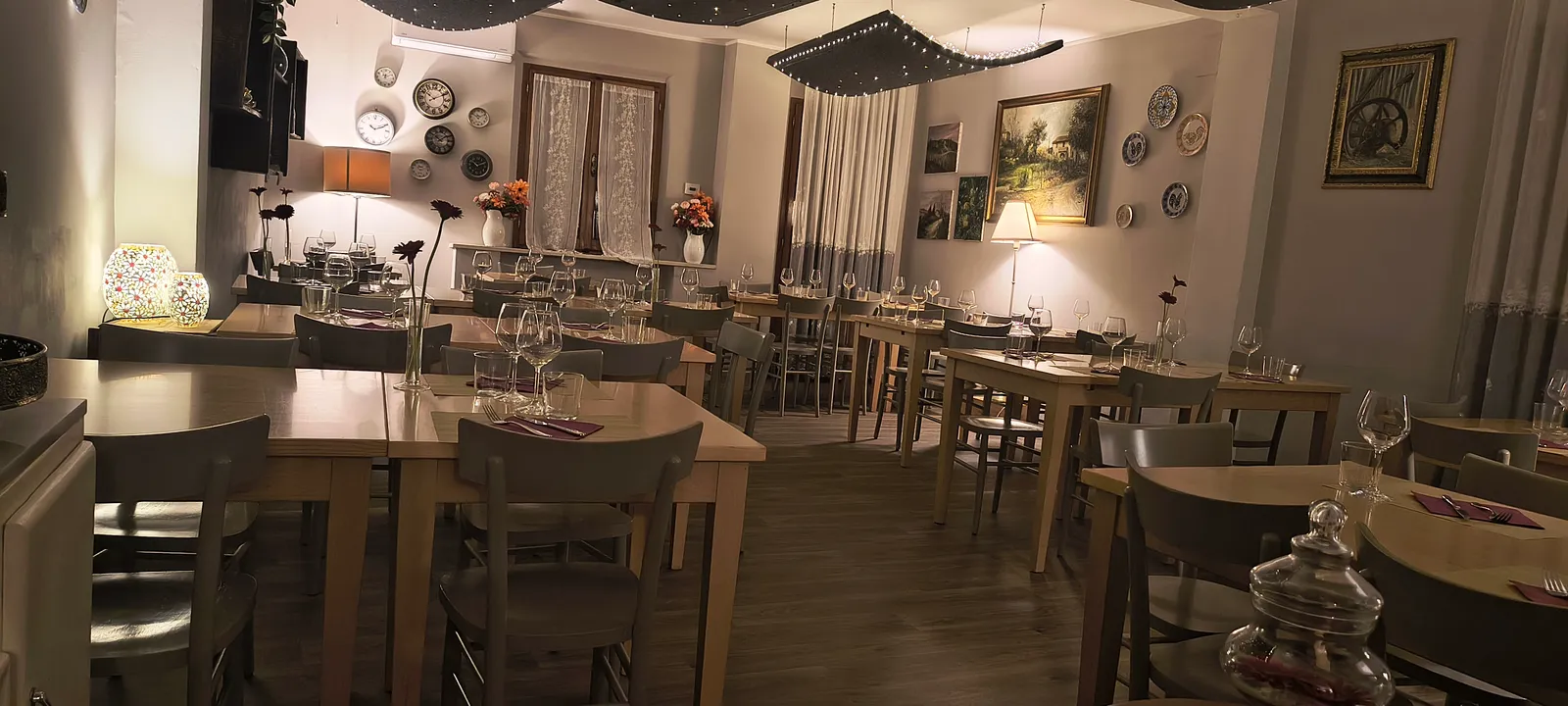 La sala illuminata la sera, vista dal fondo con i tavoli di legno