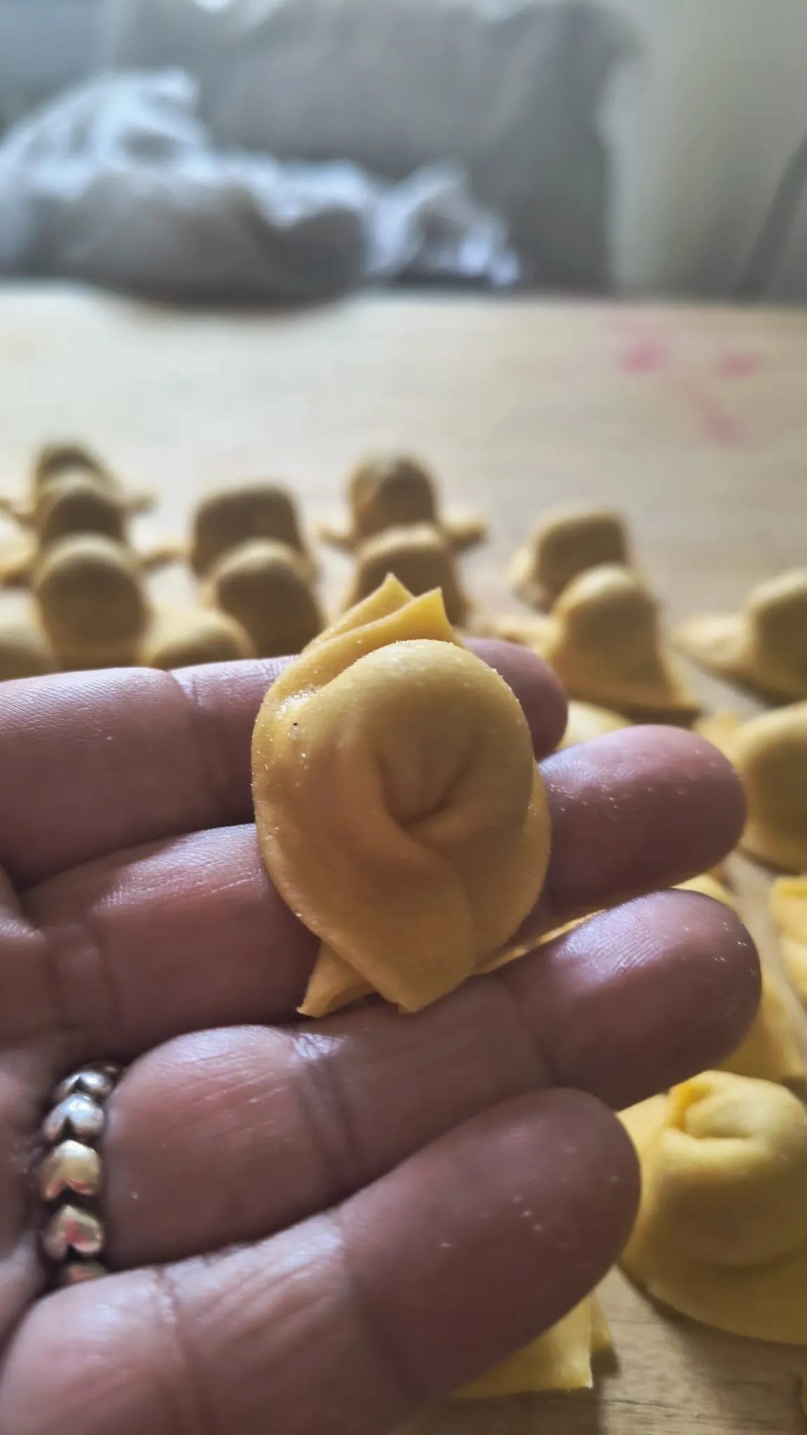 Un tortello fresco tenuto in mano, con altri tortelli sullo sfondo